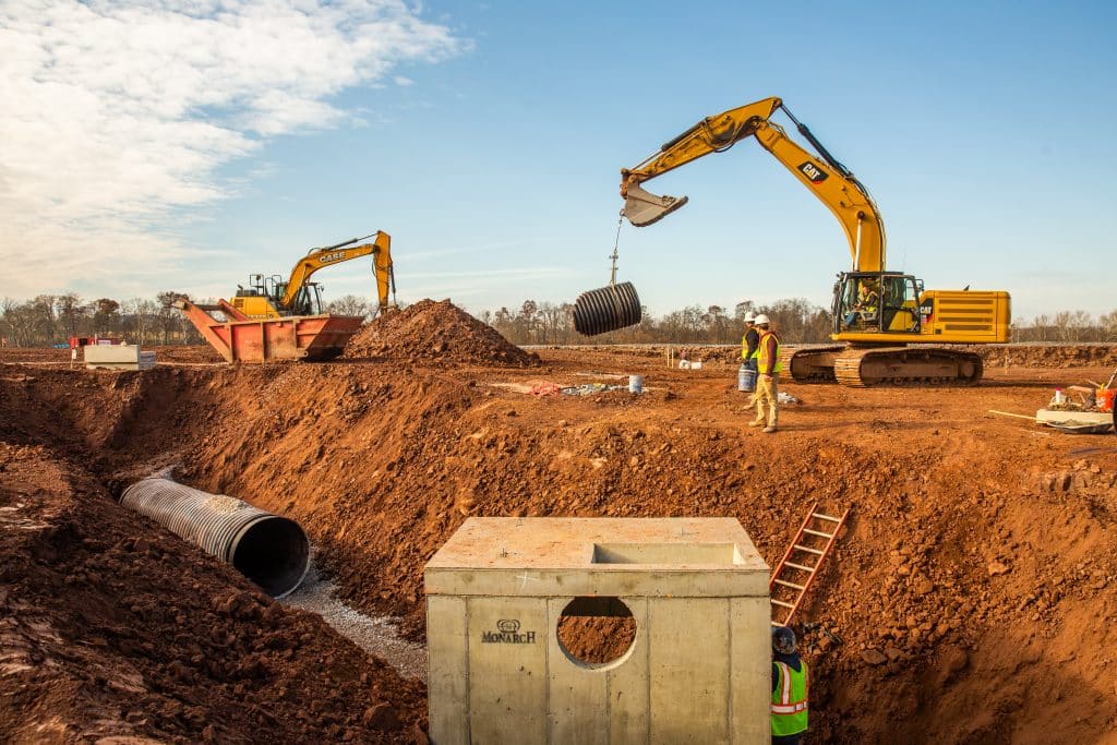 Excavator placing pipe in a precast box culvert on an active job site